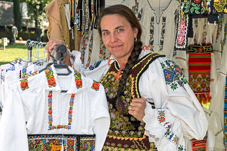 Beautiful local woman from Romania holding a blouse named "ie" - a white blouse with colorful stitches(red, green, blue)